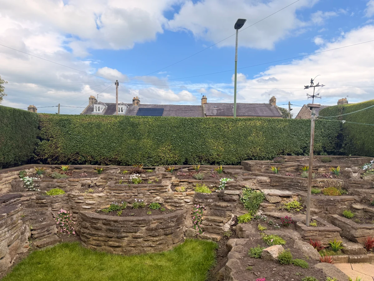 Evenly trimmed garden hedge above tiered stone borders and a lawn