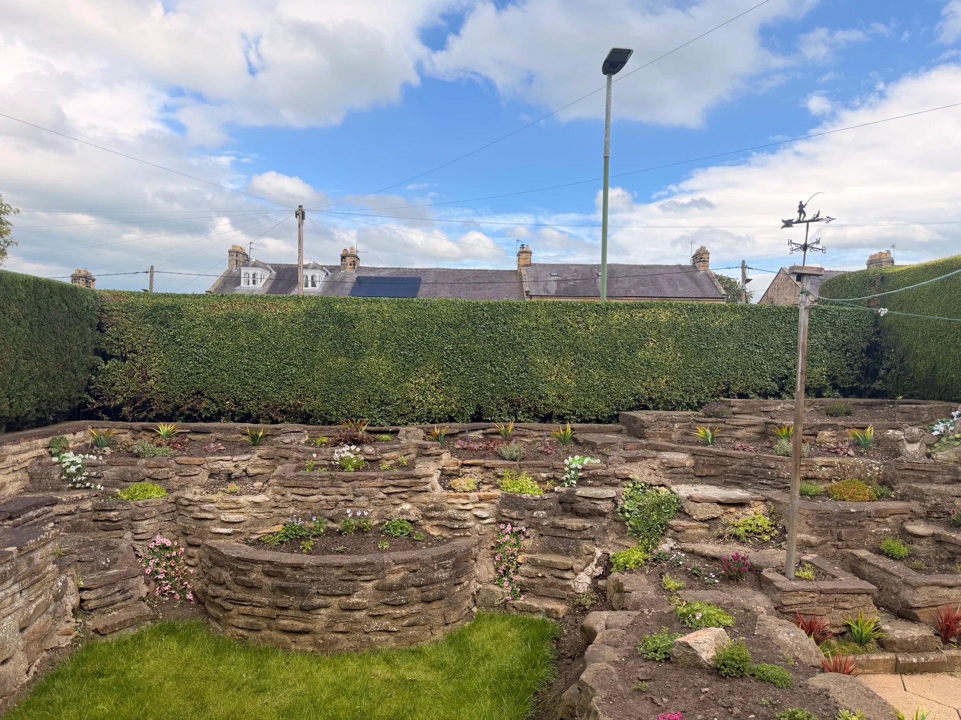 Evenly trimmed garden hedge above tiered stone borders and a lawn