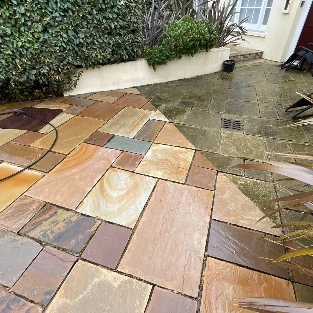 Patio during pressure washing, with cleaned paving beside the darker untreated section